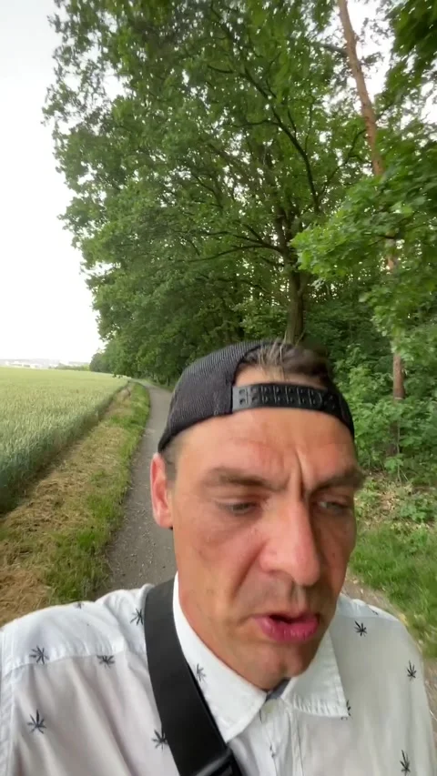 Man speaking on handheld selfie while walking along tree-lined rural path Vidéo 344586242