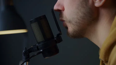Man speaking into microphone on boom arm against dark background Stock Footage 329936031