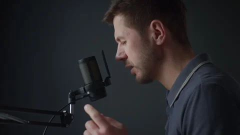 Man speaking into studio microphone against dark background Stock Footage 329936094
