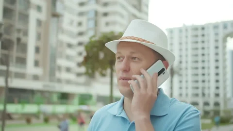 A man speaks on a mobile phone while standing on a city street Stock Footage 153869224