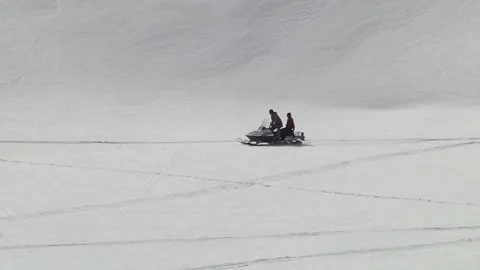 Man speeding a snowmobile on top of a mountain with a  girl behind him as a Stock Footage 145636643