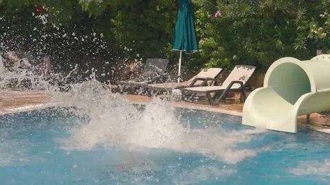 A man speeds down a water slide and fly into a pool with a huge splash Stock Footage 323844152