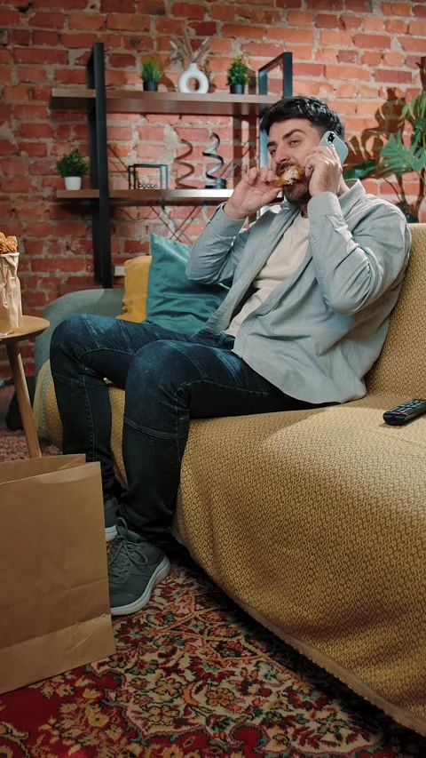Man spending time at home with fast food delivery, sits on couch eating friend Stock Footage 305496283