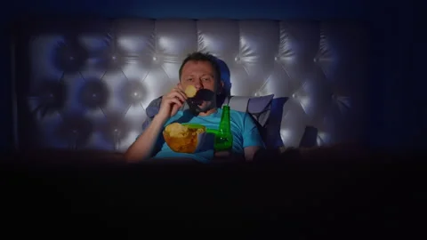 A man spends the evening at the TV with a bottle of beer and a bowl of chips 스톡 동영상 132525607