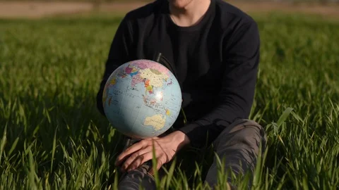 Man spinning earth globe sitting in green field Stock Footage 129082257