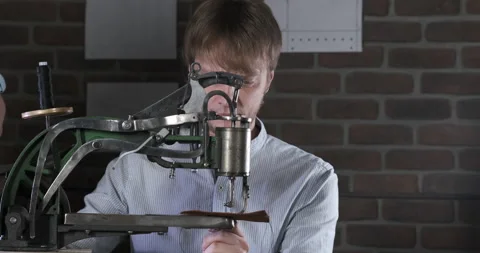 Man Spins Handle of Machine. Controlling Antediluvian Sewing Machine. Leather Stock Footage 148312857