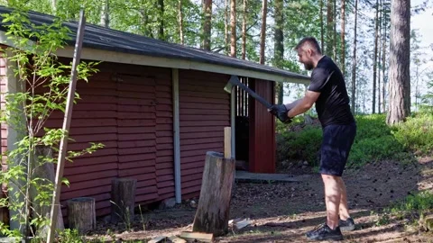 A man splits logs with an axe on a wooden chopping block. Stock Footage 338412700