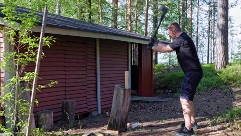 A man splits logs with an axe on a wooden chopping block. Stock Footage 338412718