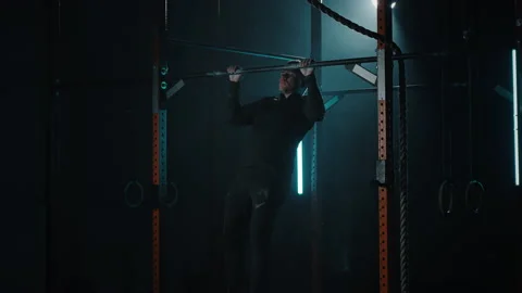 Man in sport gym pulls himself up on horizontal bar and shakes muscles Stock Footage 194045127