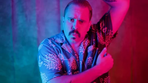 A man sporting a mustache is confidently posing in vibrant and colorful studio Vidéo 284797704