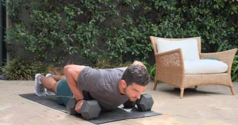 Man in sportswear doing push-ups starting lowered on mat on brick patio with Stock Footage 335199895