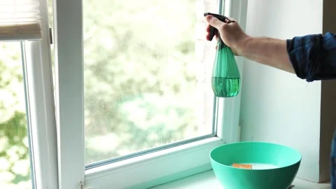 Man spraying detergent on a window with a blue basin and cleaning supplies .. Vídeos de archivo 340159433