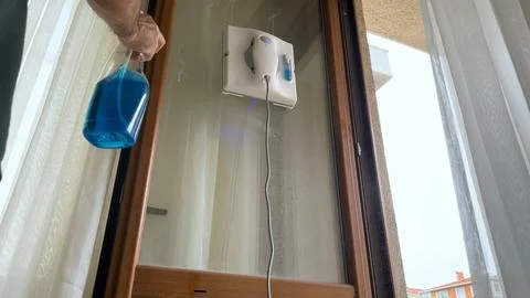 Man sprays cleaning agent on window and starts the cleaner. Robot cleans the  Stock Photos