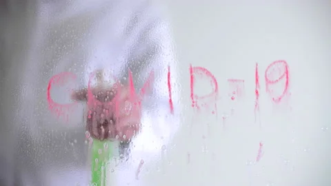 Man sprays a liquid to remove a Covid-19 symbol from a glass board Stock Footage 231056401