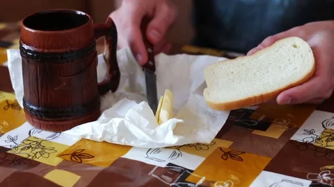 Man is spreading butter on a bread next to a cup of hot coffee Stock Footage