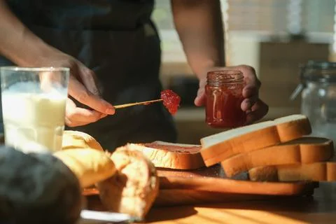 Man spreading sweet raspberry jam on toast and having breakfast at home. Stock Photos