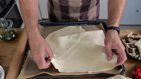 A man spreads pizza dough on a baking sheet, pressing and rolling it thin w.. Video stock 285024799