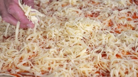 A man sprinkles grated cheese over tomato-sauced pizza dough in a home kitc.. Vídeo Stock 286309847