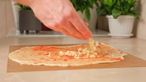 A man sprinkles mozzarella cheese on layer of yeast dough, basis for pizza Stock Footage 244677975