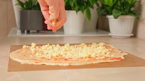 A man sprinkles mozzarella cheese on layer of yeast dough, basis for pizza Stock Footage 244678231
