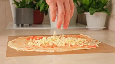 A man sprinkles mozzarella cheese on layer of yeast dough, basis for pizza Stock Footage 245657163