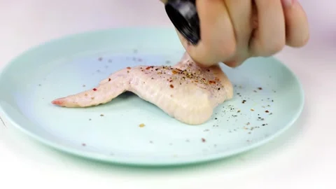 A man sprinkles pepper on raw chicken meat. Stock Footage 160506740