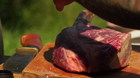Man sprinkling salt over a raw rib eye steak on a wooden board Stock Footage 250158014