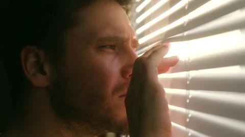 Man spying through blinds, observing from window Stock Footage 296550625