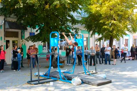 A man in the square does gymnastic exercises on uneven bars and a crossbar. D Stock Photos