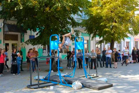 A man in the square does gymnastic exercises on uneven bars and a crossbar. D Stock Photos