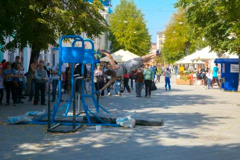 A man in the square does gymnastic exercises on uneven bars and a crossbar. D Stock Photos