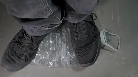 A man squashing a plastic bottle with his feet in shoes. Stock Footage 135593403