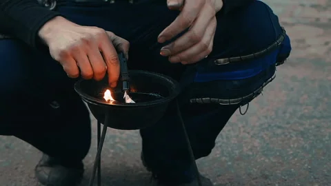 The man squats and lights a fire in the bowl before the fire show begins. Stock Footage 160759882