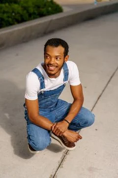 Man squatting and posing in overalls and white shirt Stock Photos