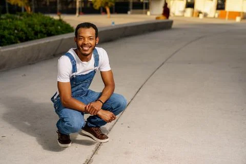 Man squatting and posing in overalls and white shirt Stock Photos