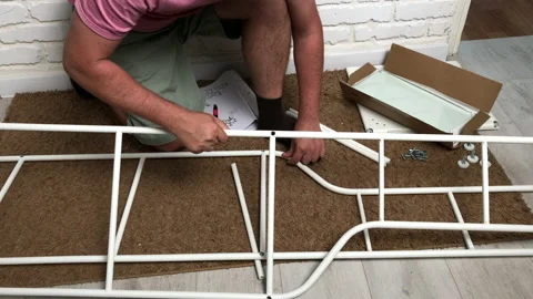 A man squatting, assembles a rack. Connects elements with fasteners. Homework 動画素材 157187027