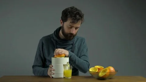 Man with Squeezer Squeezing and Drinking Orange Juice, Grey Background Stock Footage 76521813