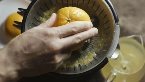 Man squeezes juice from an orange on a juicer Stock Footage