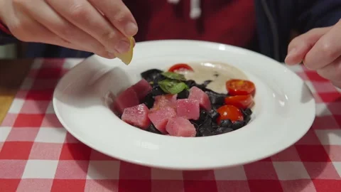 A man squeezes lemon juice on raw tuna. Italian cuisine: black pasta with Stock Footage 161421385