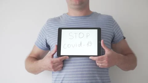 A man squeezes a tablet screen with the inscription STOP Covid-19 to the camera Stock Footage 134588289