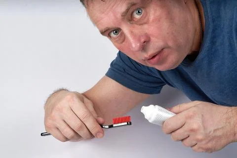 Man squeezes toothpaste onto black toothbrush with red shield Stock Photos