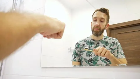 A man squeezes toothpaste onto the brush and brushes his teeth in a bathroom Stock Footage 301512332