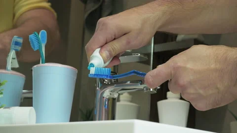 Man squeezes toothpaste onto a toothbrush in front of a bathroom mirror Stock Footage 213581436