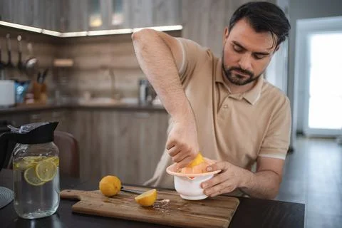 Man squeezing lemons in the kitchen preparing detox water or lemonade Stock Photos