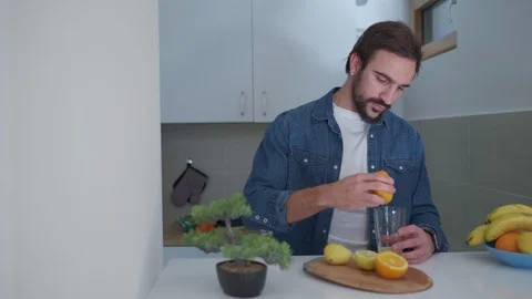Man squeezing orange in to a glass in the kitchen 스톡 동영상 127648967