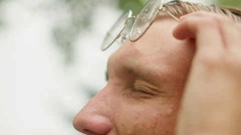Man squints amid rainy park, Young man with wet glasses and strained expression Stock Footage 329442927