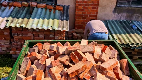 Man stacking damaged red bricks into green trailer near storage wall piles Stock Footage 312718819