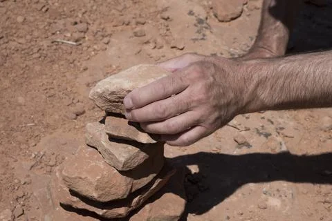 Man stacking rocks on the side of the trail in the desert to create a cairn. Stock Photos