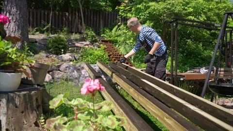 Man staining wooden beams with roller brush outdoors on a sunny day. Stock Footage 311925374