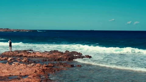Man stand on big stone and take a photo of blue sea waves Stock Footage 211174820